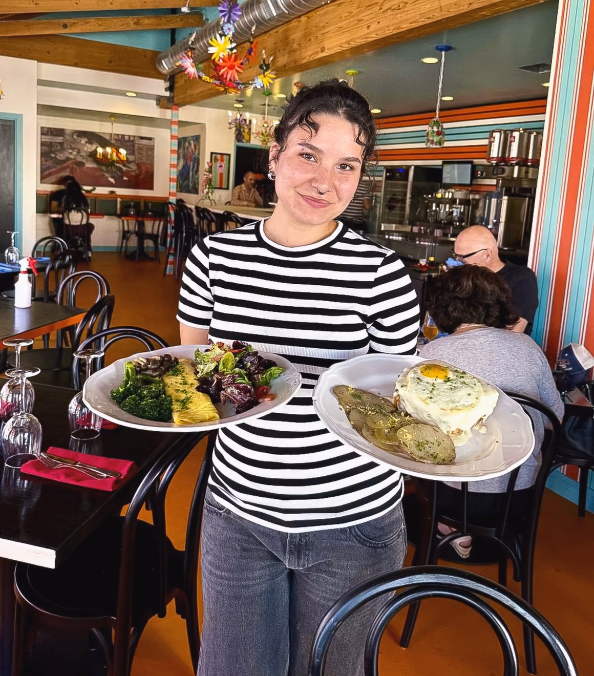 A smiling server carrying an omelette and a croque madame through the colorful dining room